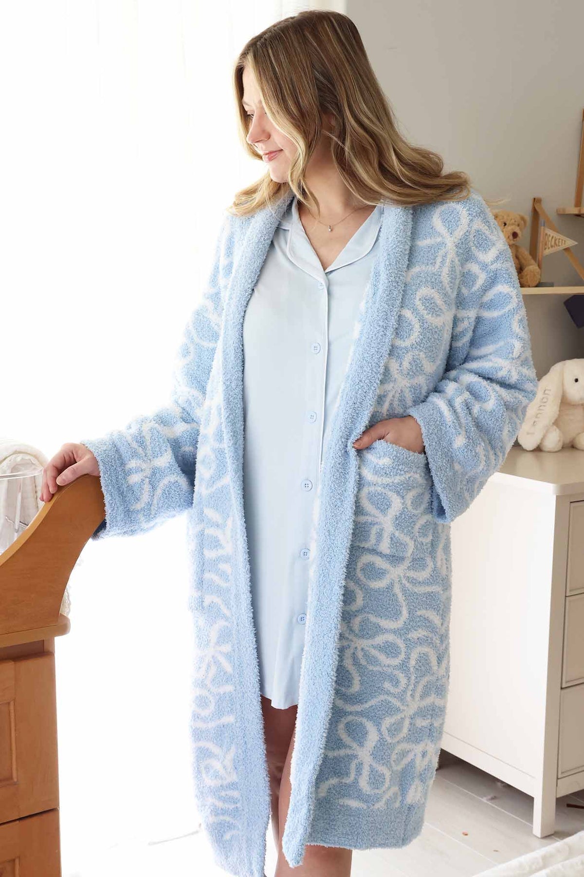 mom standing next to bassinet in baby blue labor & delivery gown with a plush blue and white bow robe