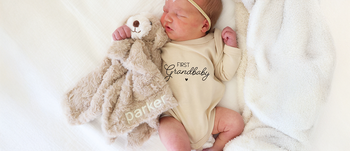 Baby wearing a first grandbaby graphic bodysuit with a personalized animal lovey from Caden Lane