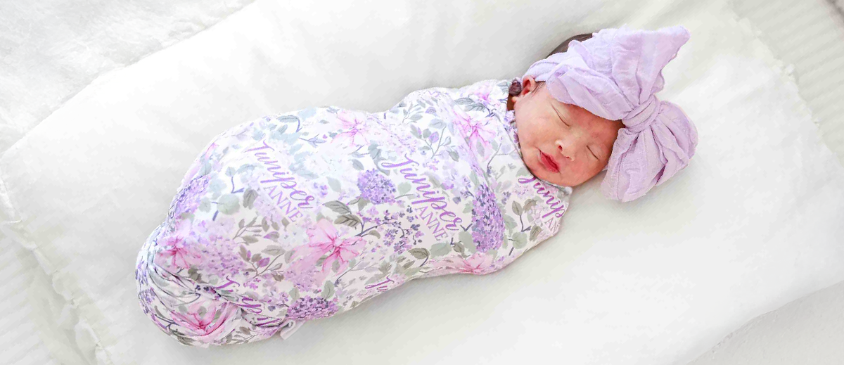 Baby wearing Caden Lane lavender floral swaddle and bow