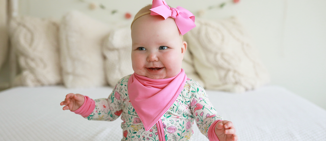 Baby girl wearing Caden Lane's pink bandana bib and floral zip romper