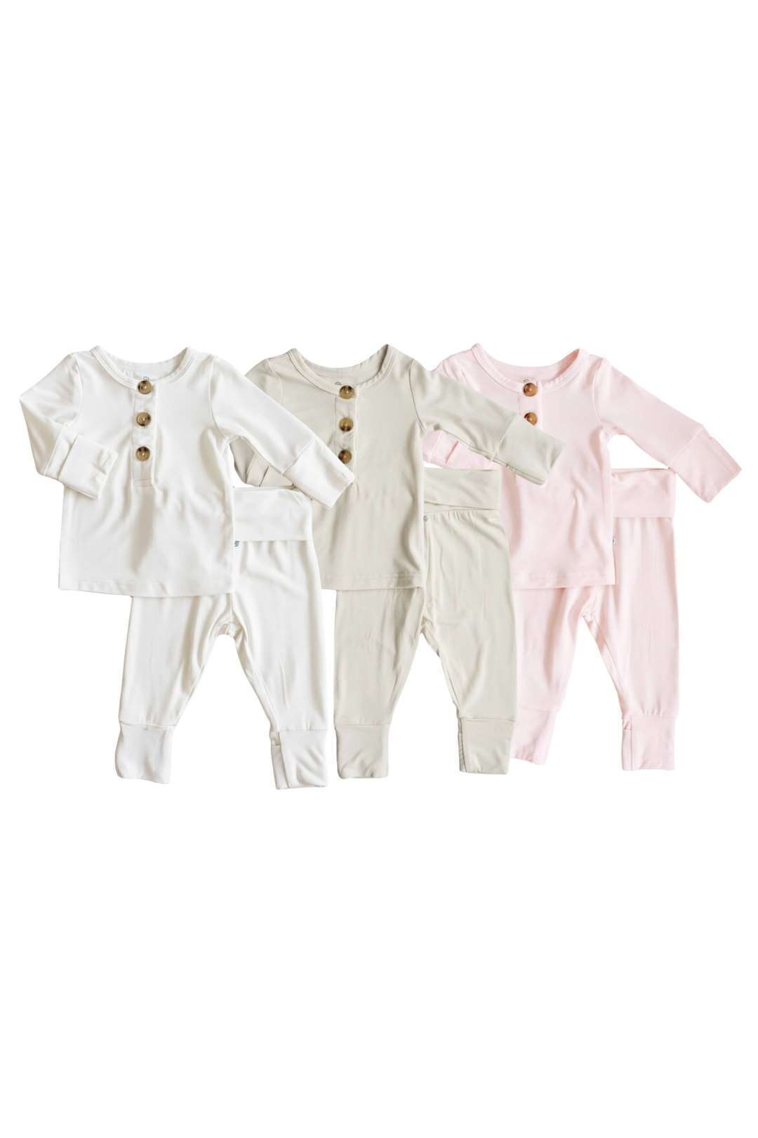 Three Caden Lane baby long-sleeve 2 piece outfits with buttoned style fronts, shown side by side on a plain white background. The set includes off-white, light beige, and pale pink versions, each with three wooden buttons at the chest.