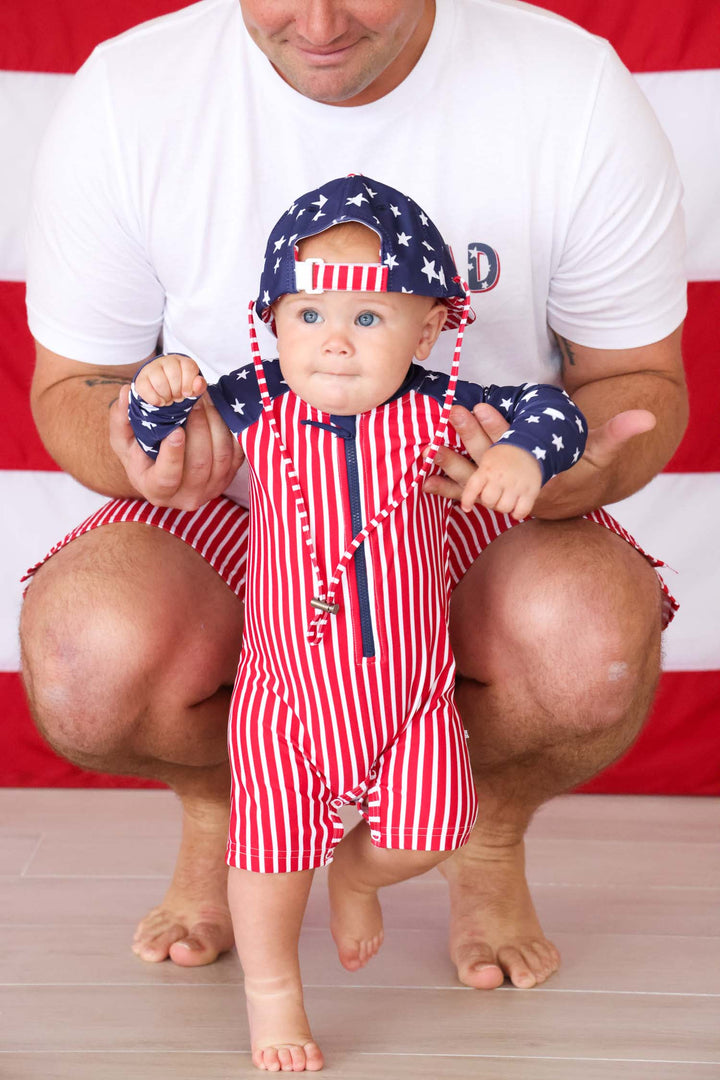 standing baby boy in stars & stripes swim romper shortie and matching surf hat 