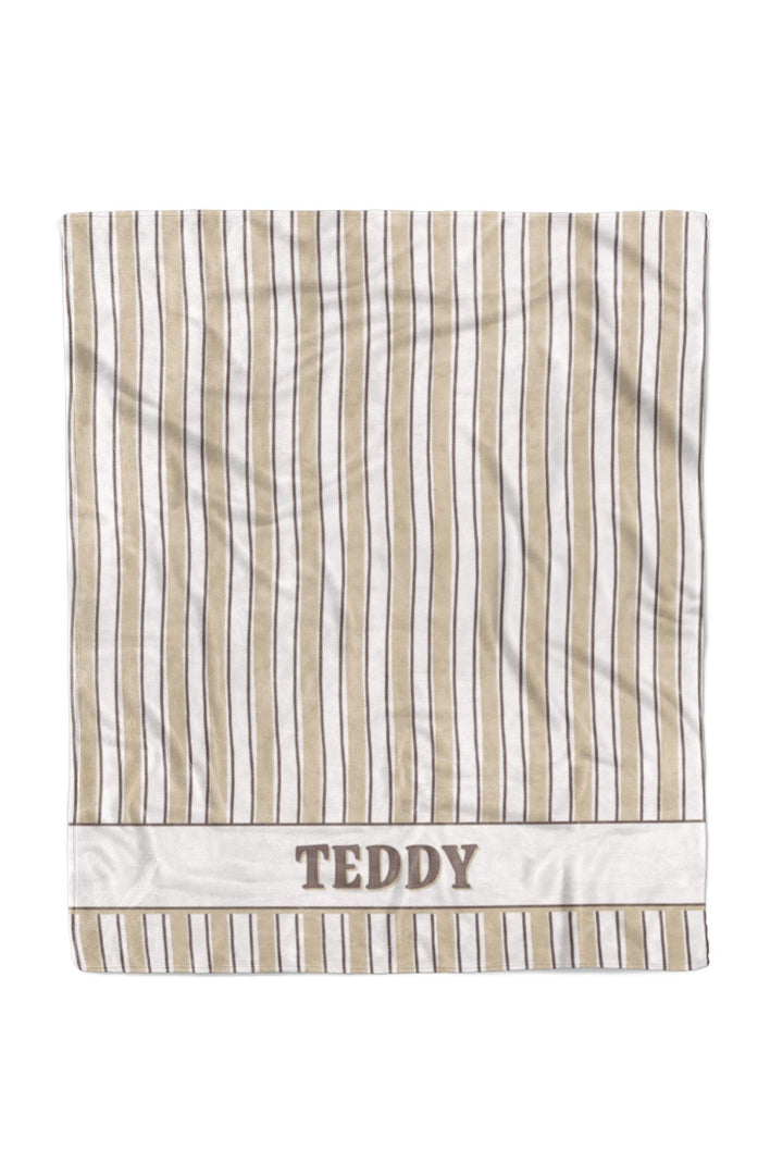 Flat-lay of personalized 50x60 pet blanket in Biscuit Stripe pattern with tan and white vertical stripes, featuring the name TEDDY embroidered on a white border at the bottom