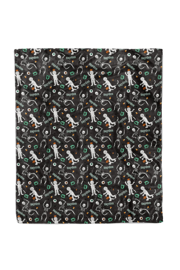 Close-up of black blanket fabric personalized with the name 'Hayden' repeated throughout, along with Halloween skeleton graphics.
