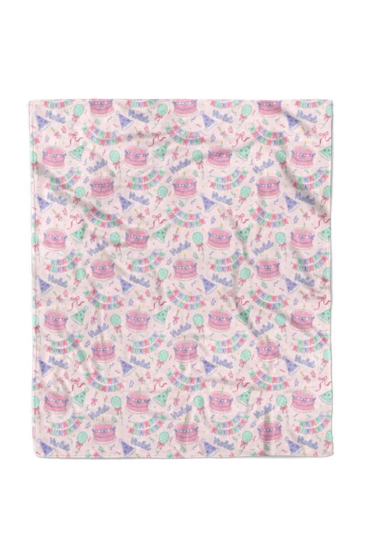 A Caden Lane personalized blanket with child's name and 'HAPPY BIRTHDAY' text on a light pink background.