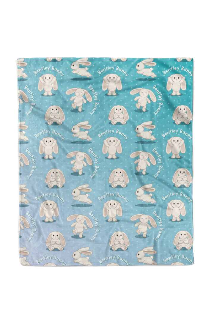 Flat lay of a Caden Lane personalized "Bentley Bunny" fleece baby blanket in a teal-to-blue ombre polka dot pattern, covered in a repeating print of a bunny character in different poses with "Bentley Bunny" text arched throughout.