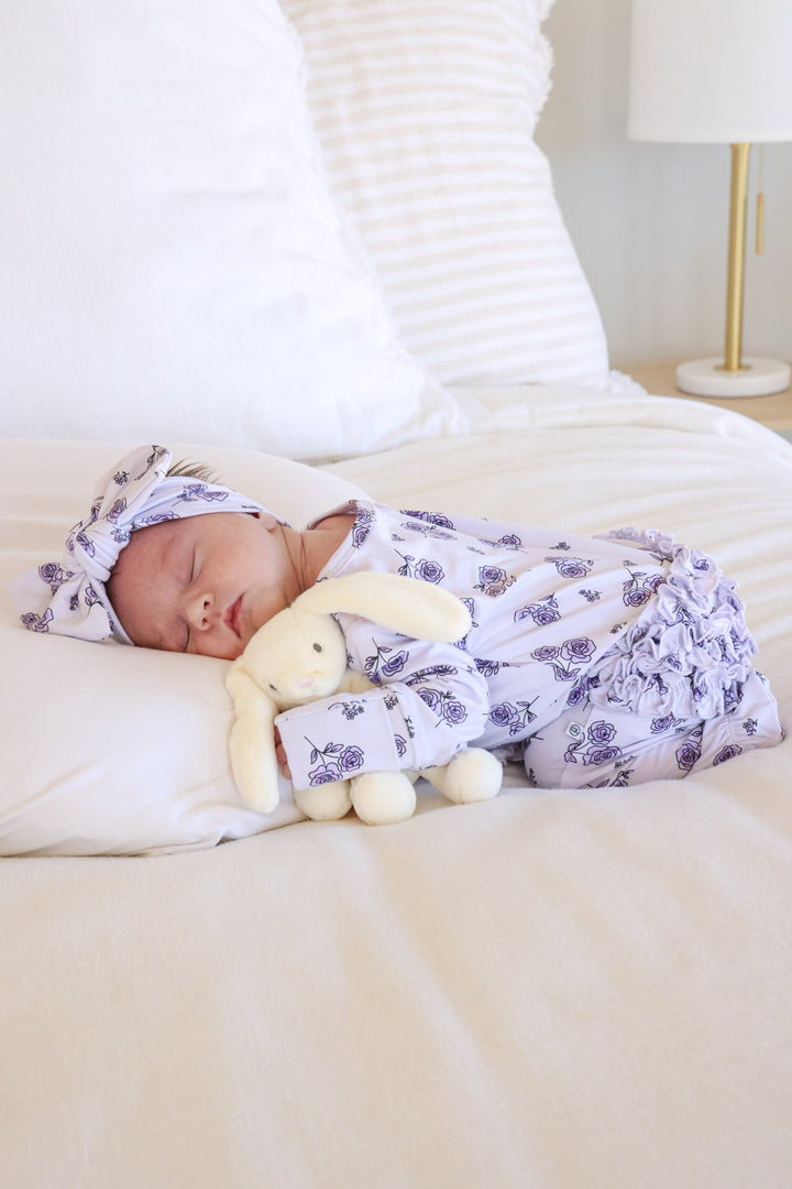 baby girl laying on stomach in amethyst garden ruffle zipper footie with matching headwrap and mini bunny 