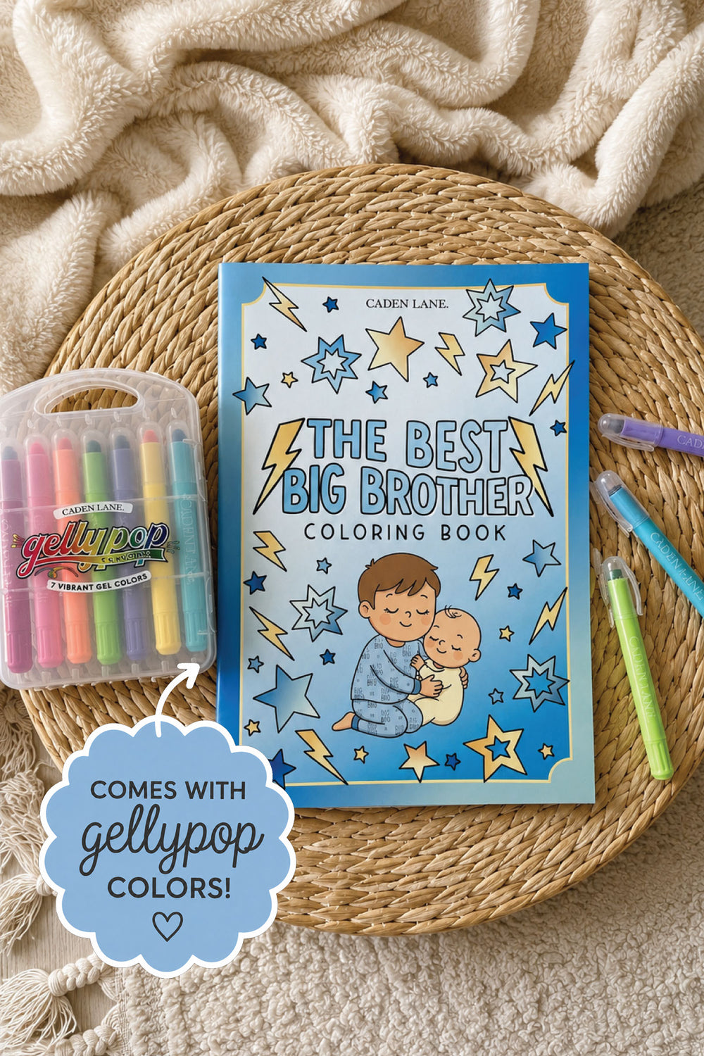Flat lay of a Caden Lane blue coloring book reading "The Best Big Brother" with stars and lightning bolts on a woven seagrass mat, paired with Gellypop gel crayons.