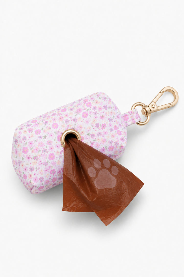 Scattered Blooms pet waste bag holder showing a waste bag being dispensed from the bottom, with gold carabiner clip at top
