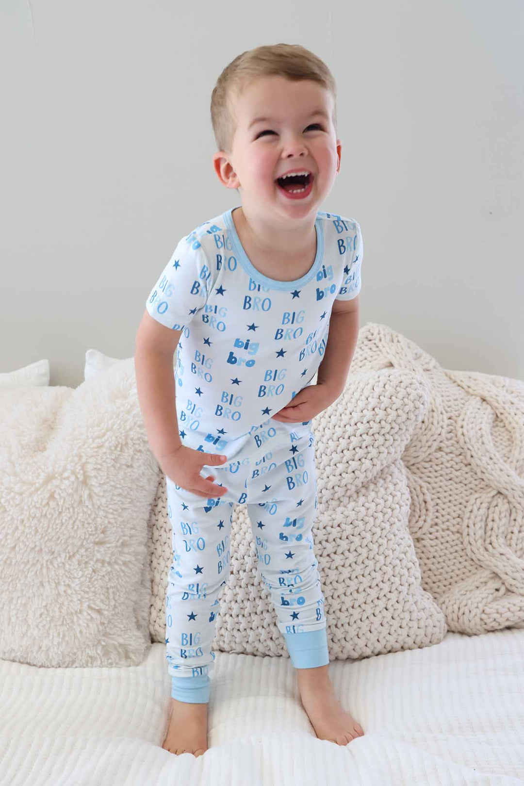 boy laughing standing on the bed wearing short sleeve big bro two piece pajama set 
