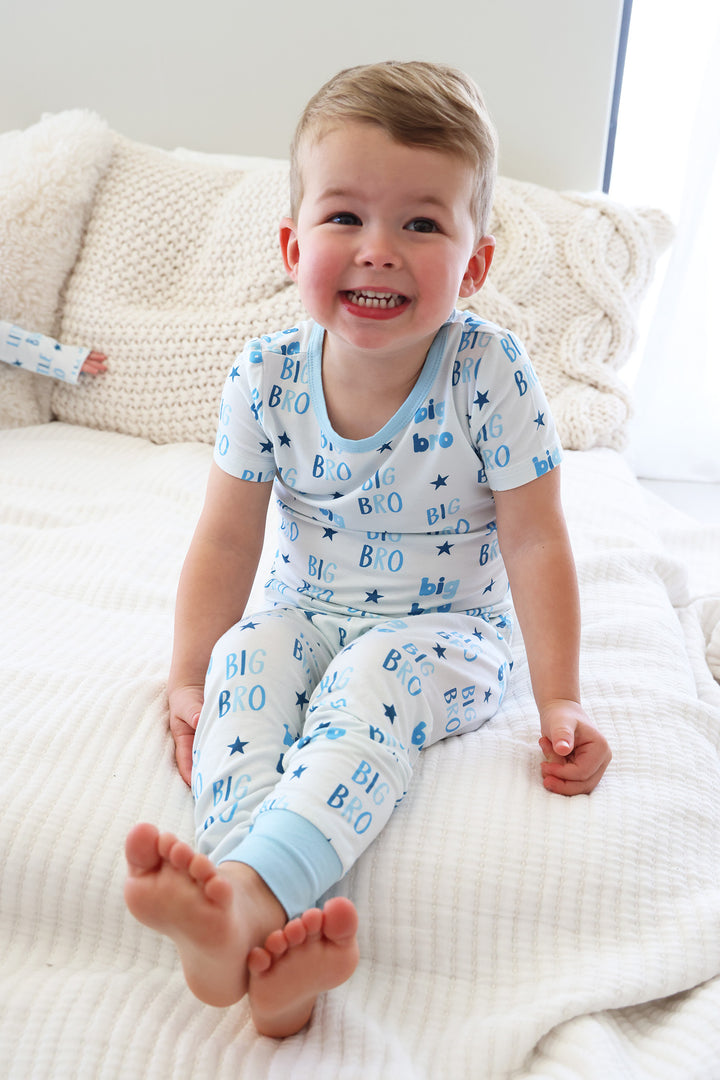 boy sitting on a bed with his legs crossed wearing the big bro star two piece pajama set 