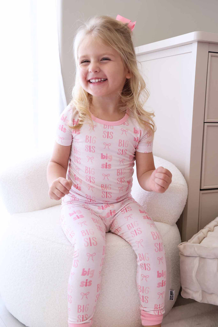 smiling girl in pink two piece short sleeve pajama set with pants in big sis print 