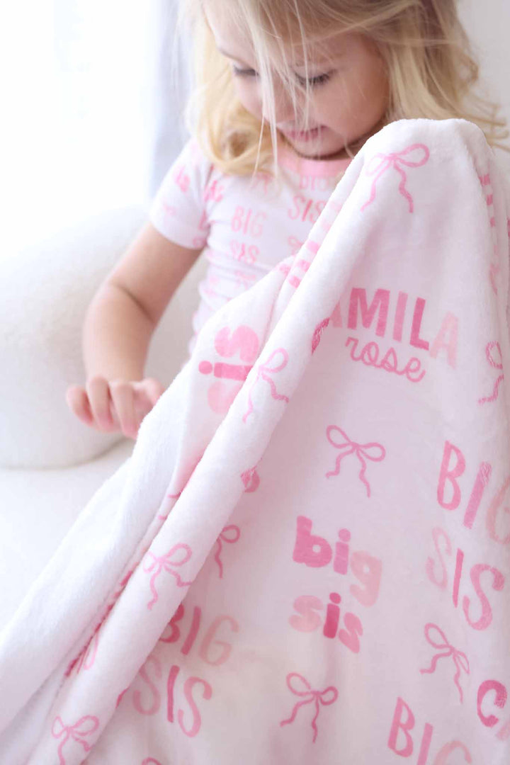 girl holding up the big sis personalized blanket for girls in pink with bows and block letters