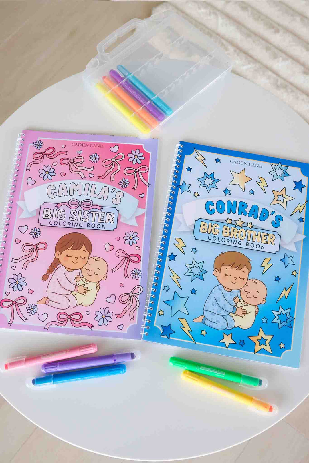 Caden Lane 'Camila's Big Sister' and 'Conrad's Big Brother' Coloring Books displayed together on a white table with a Gellypop crayon case and pastel markers