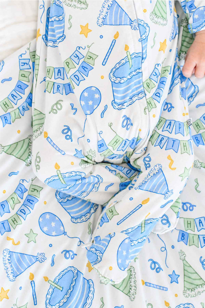 Close-up of the Caden Lane Birthday Bash Blue newborn knotted gown featuring birthday cakes, balloons, party hats and banners.
