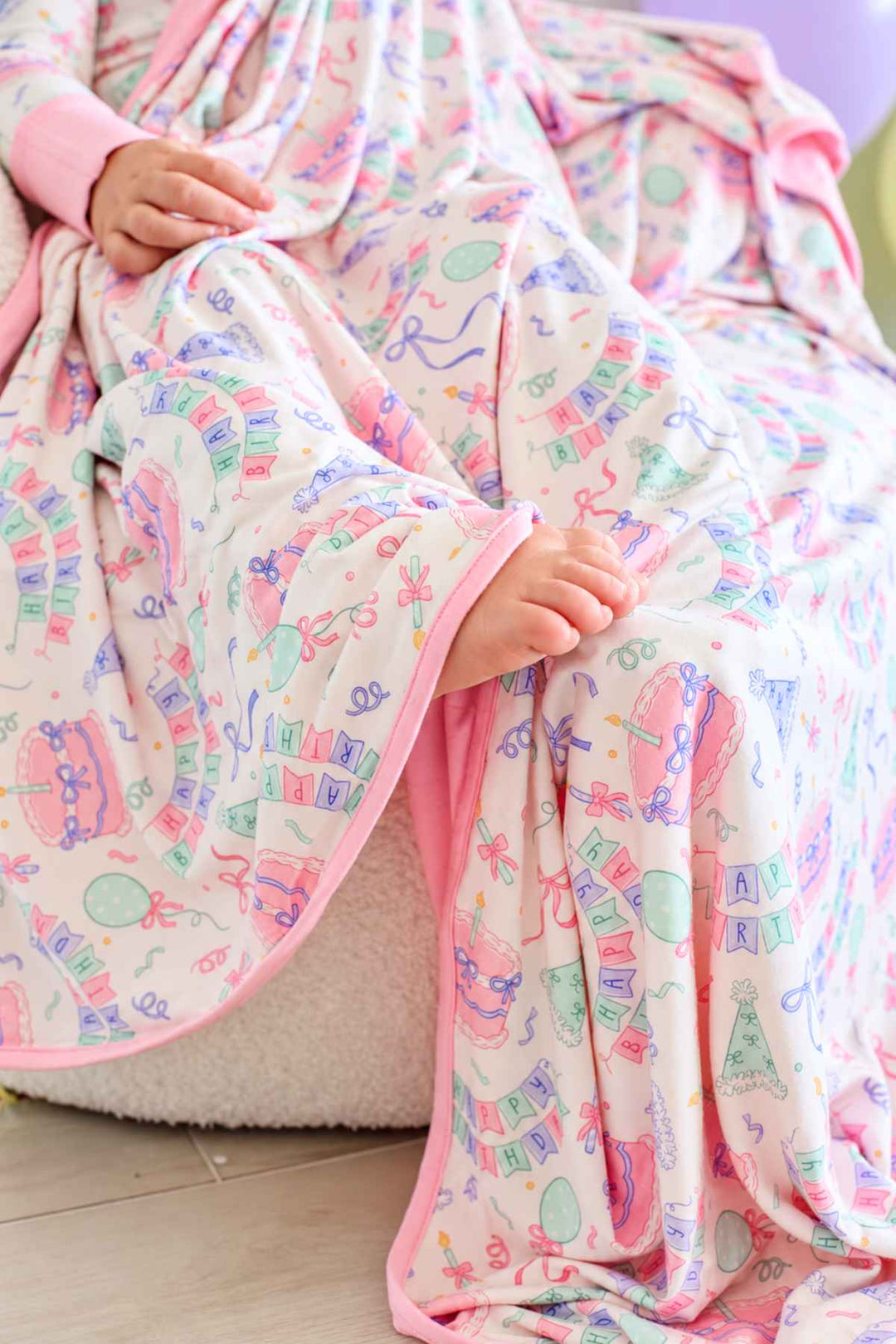 Close-up of the Caden Lane Birthday Bash Pink bamboo blanket featuring birthday cakes, balloons, party hats, confetti and pink trim.
