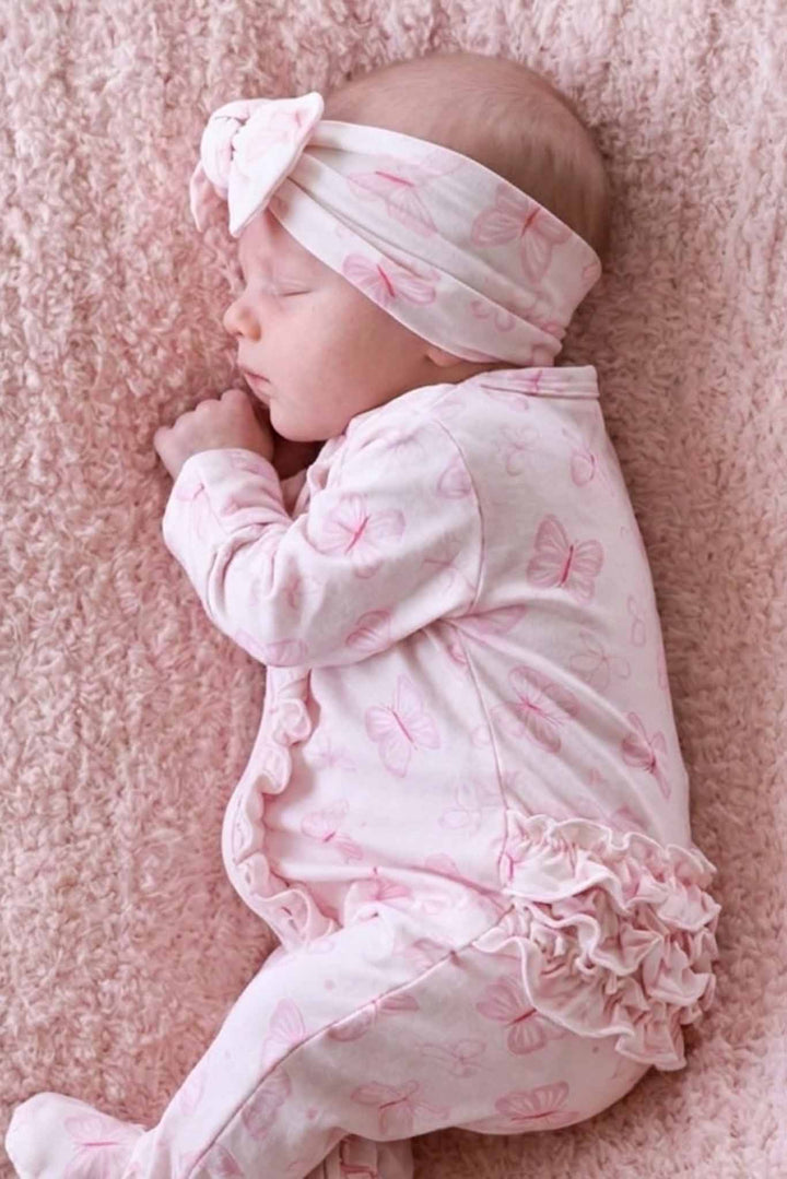 Ruffle Zipper Footie in Blooming Butterflies print - close-up lifestyle shot of newborn holding a stuffed bunny in the butterfly-print footie, with ruffled bottom hem visible at ankles