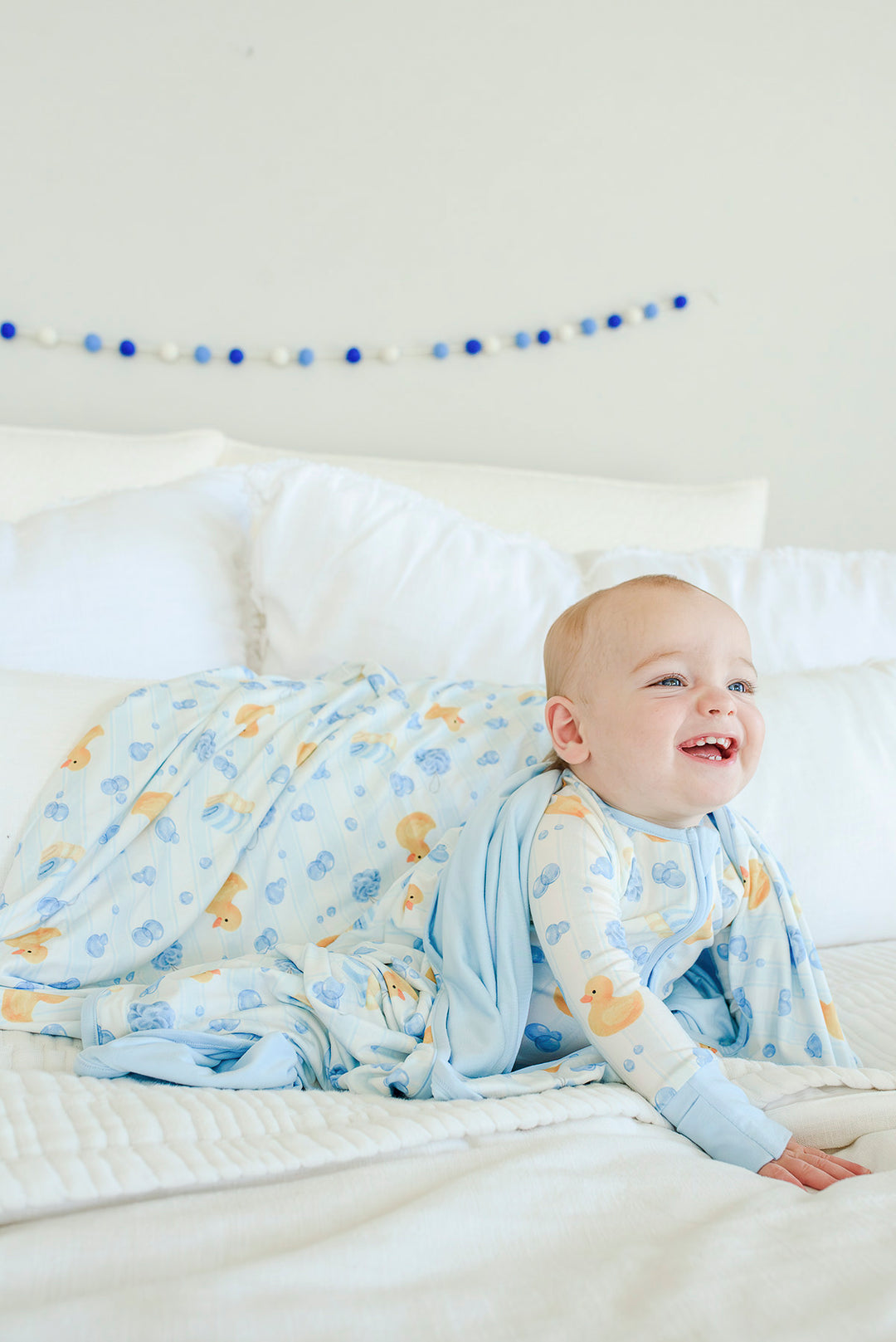 Happy baby lying on blue Bubble Duckies double-sided bamboo blanket smiling in a crib setting