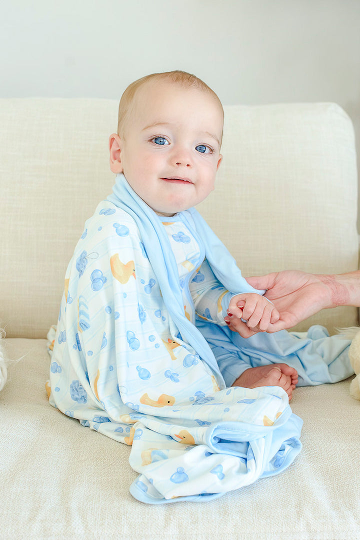 Baby sitting up with blue Bubble Duckies bamboo blanket draped around them showing yellow rubber duck and blue bubble print