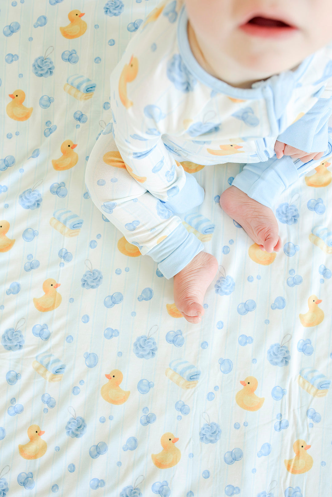 Overhead view of baby lying on blue Bubble Duckies bamboo blanket with yellow rubber duck print