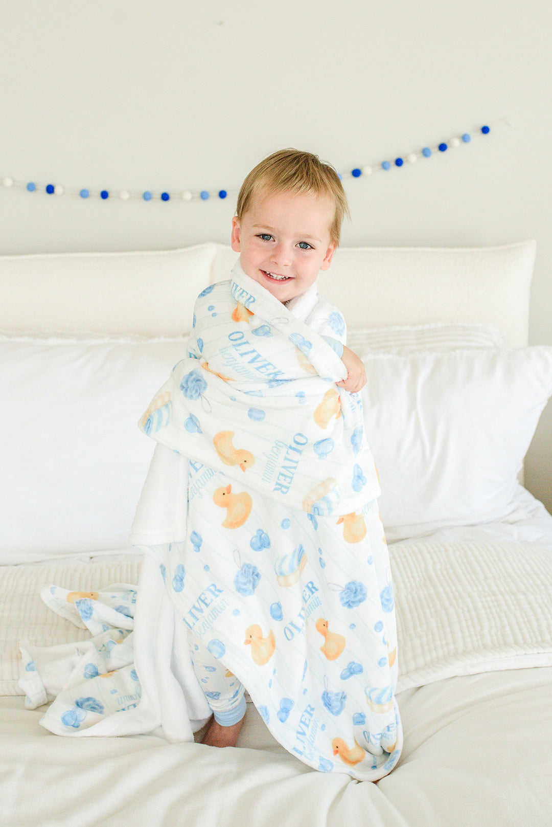 Baby boy smiling and wrapped in blue Bubble Duckies personalized blanket with rubber duck and bubble print