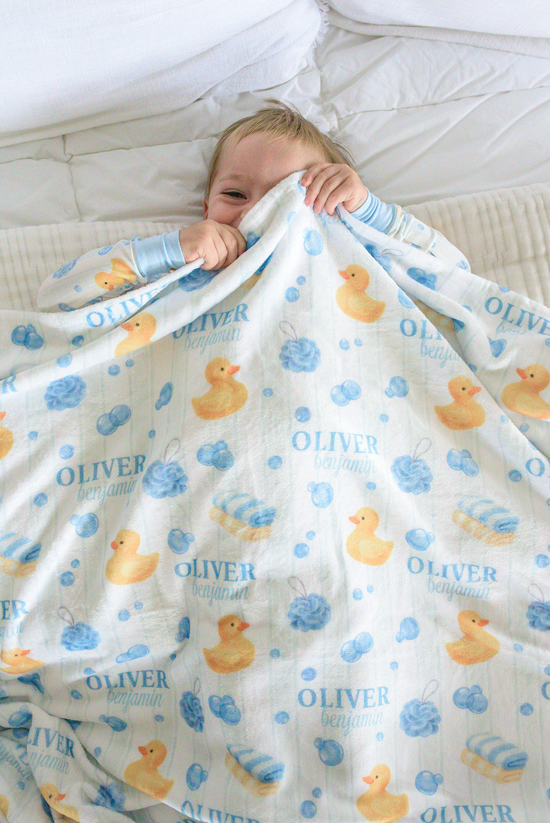 Boy looking down while wrapped in blue Bubble Duckies personalized kids blanket with duck print and custom name