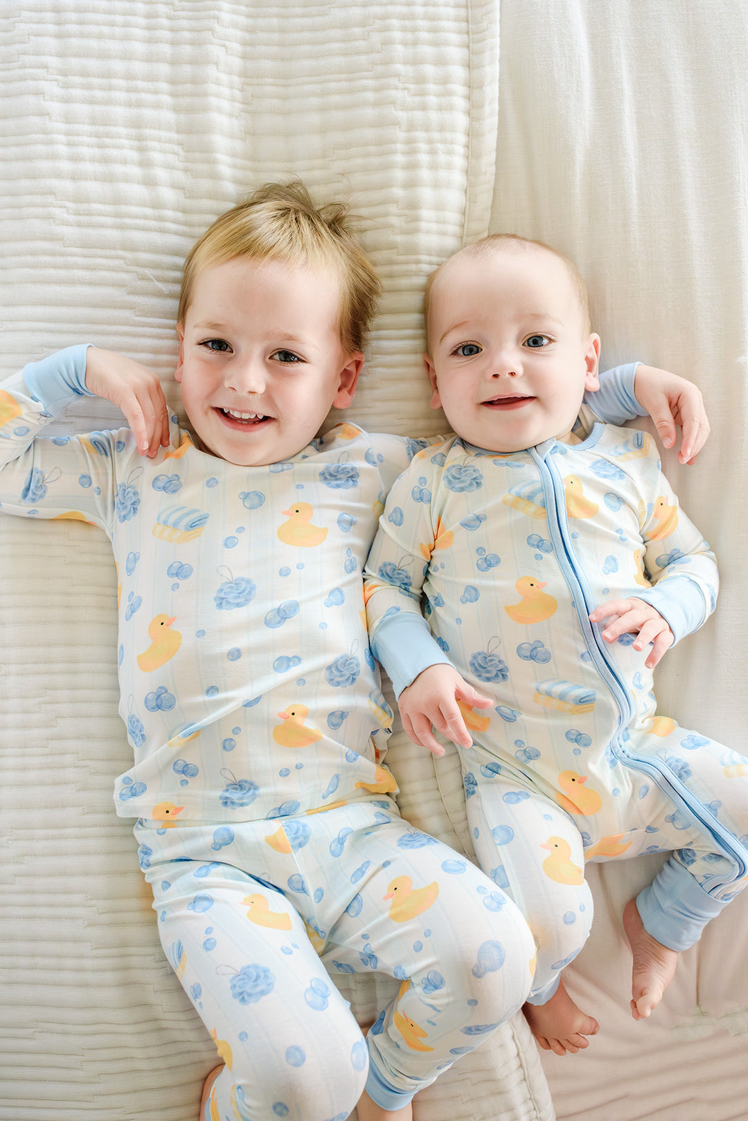 Two brothers lying together wearing matching blue Bubble Duckies bamboo pajamas with yellow rubber duck print