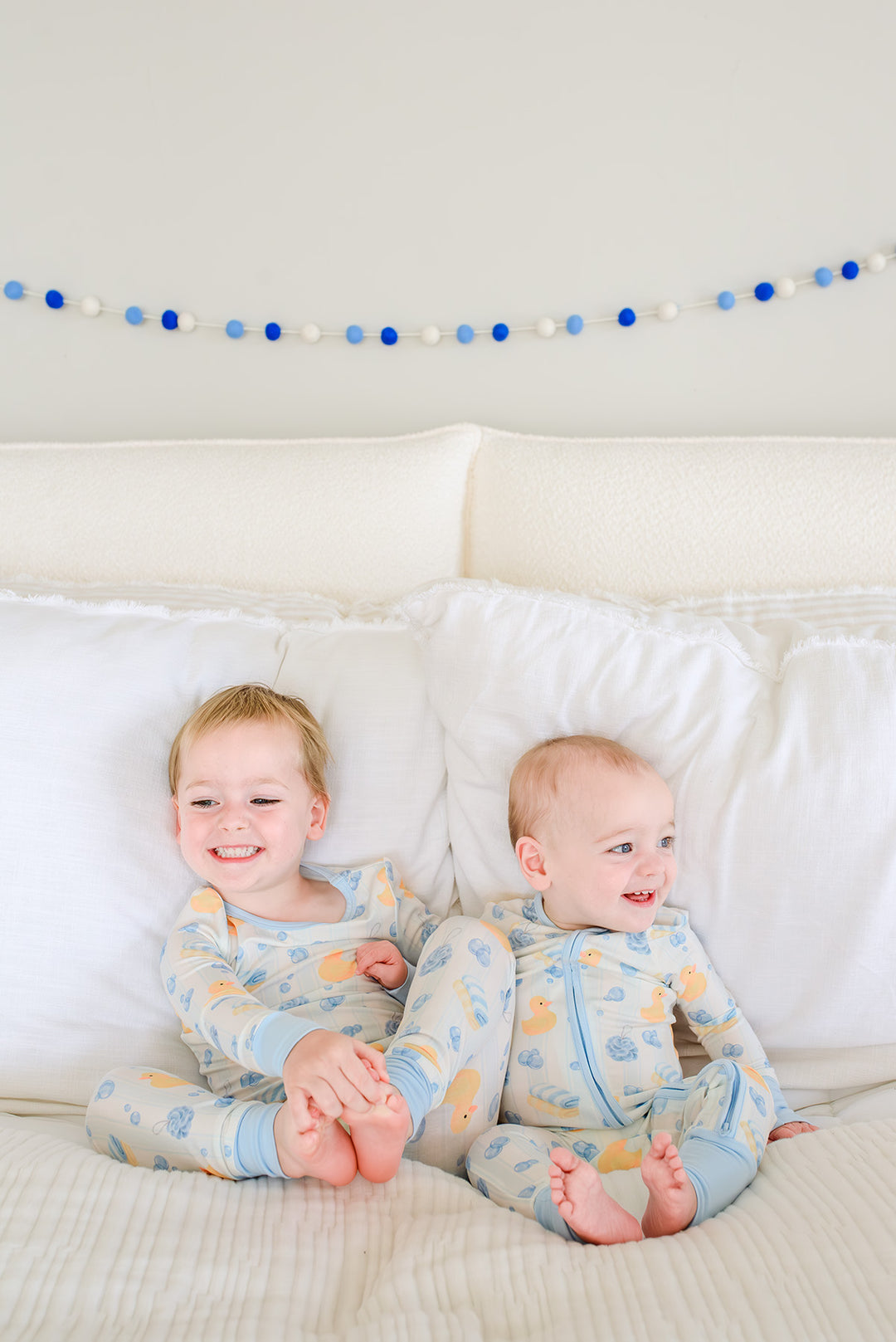 Close-up of two babies wearing blue and pink Bubble Duckies zip romper pajamas side by side with rubber duck print