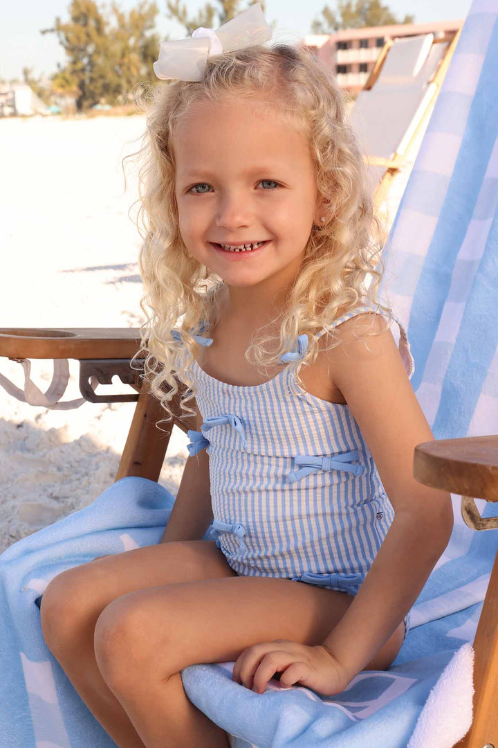 girl sitting on lounge chair in blue bow seersucker one piece swimsuit 