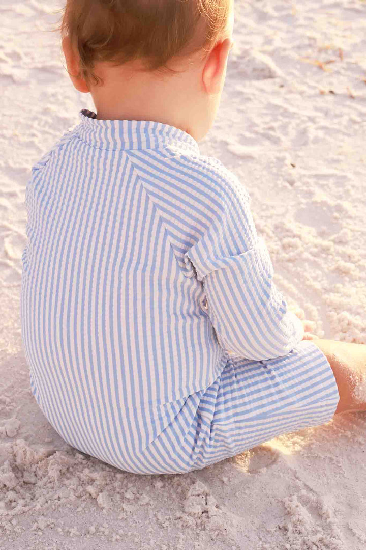 boy sitting on the beach in blue seersucker romper shortie