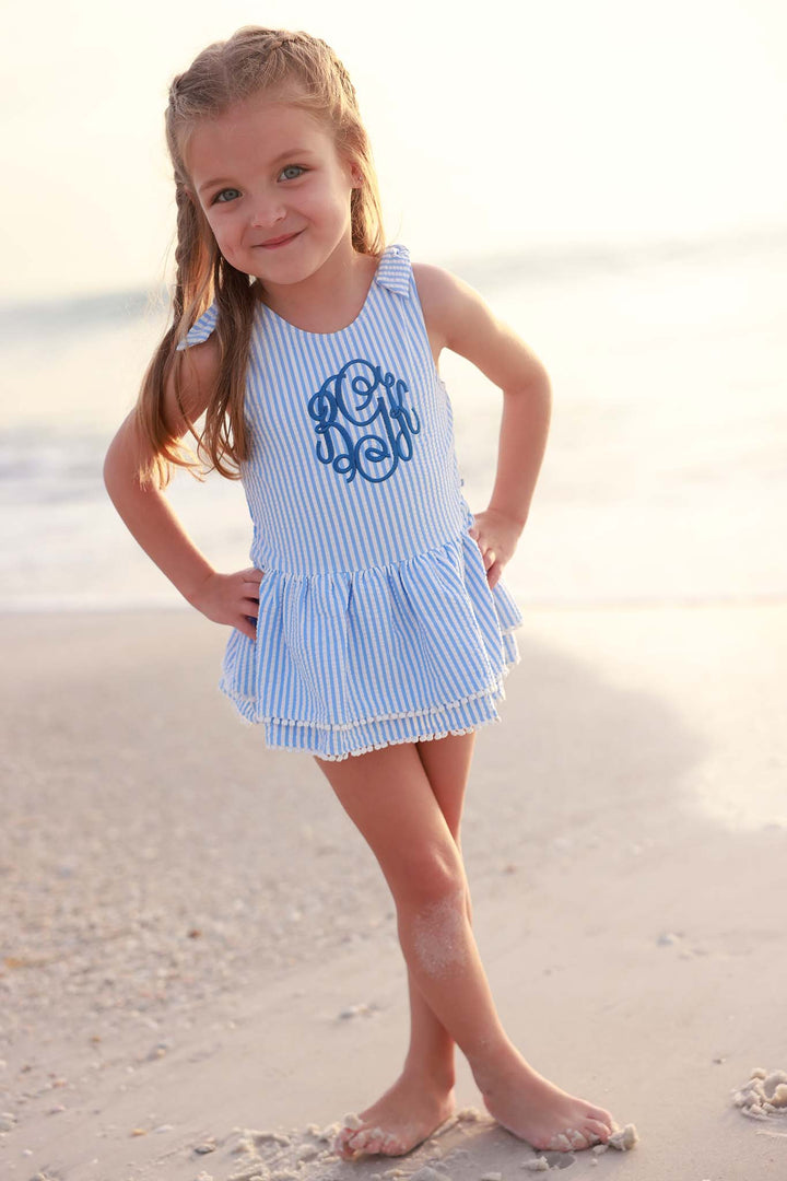 girl standing on the beach in blue seersucker skirted one piece with blue embroidered monogram 