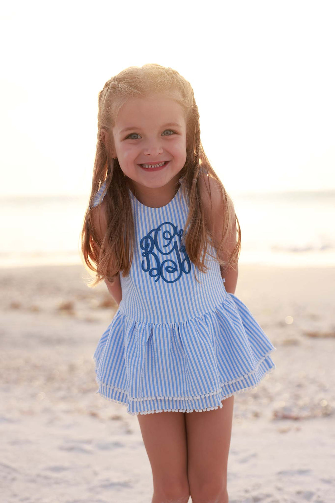 smiling girl standing on the beach in blue seersucker monogrammed one piece swimsuit 