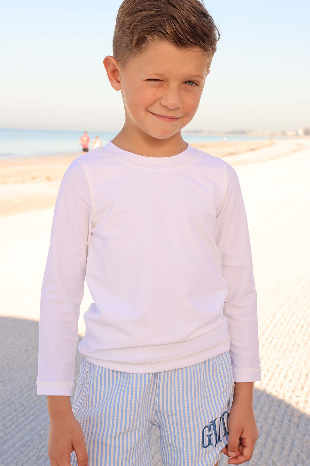 boy at beach wearing long sleeve rash guard shirt in white with monogrammed seersucker shorts 
