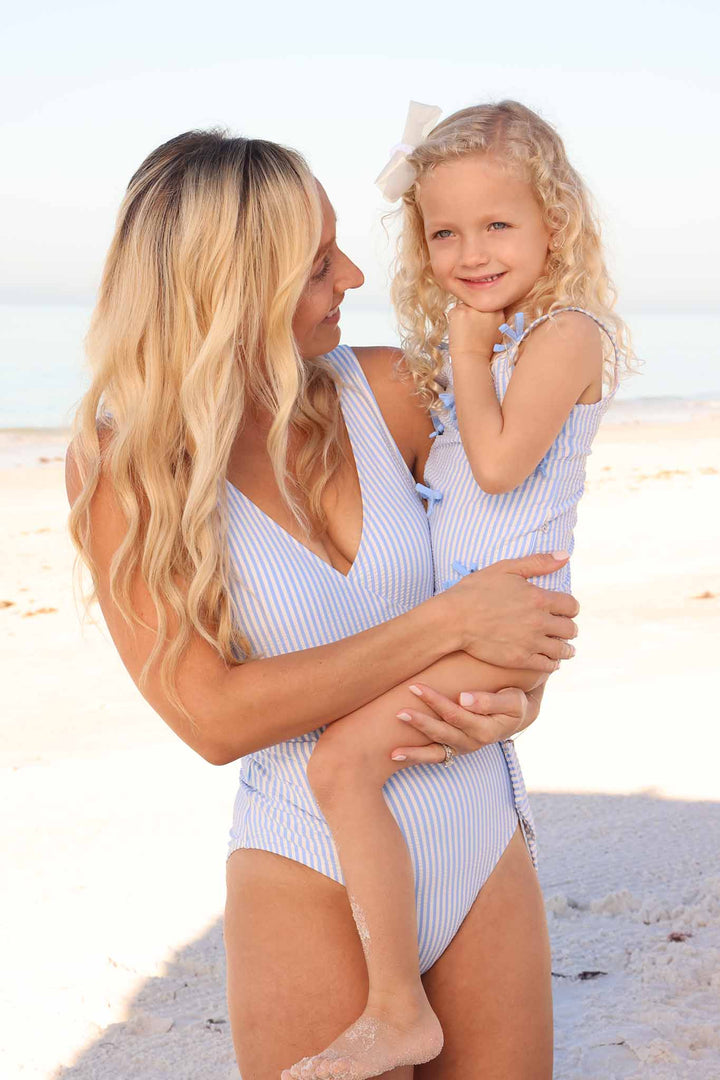 mom holding daughter on beach in matching blue seersucker swimsuits 