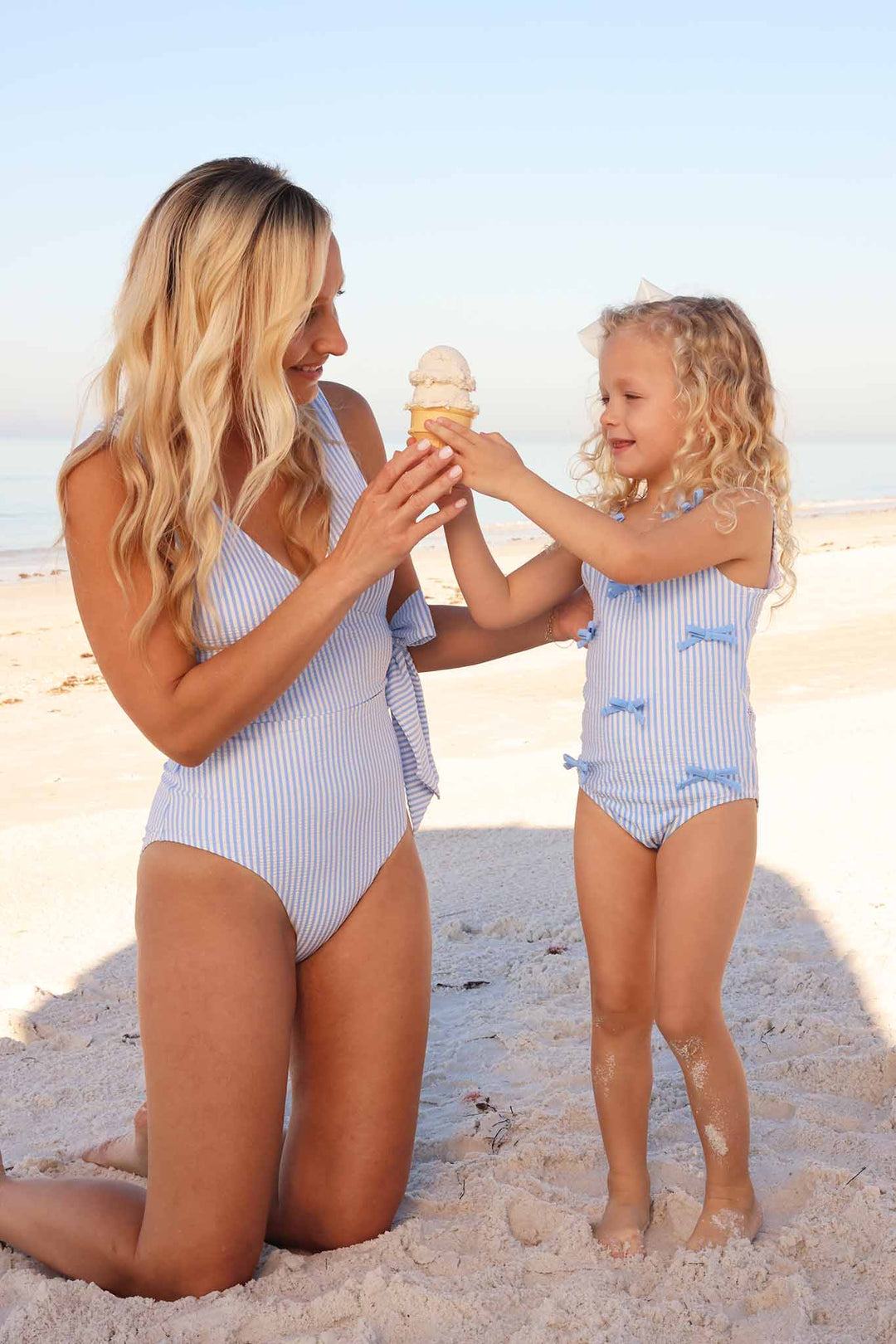 mom and daughter holding ice cream  cone on beach in matching seersucker swimsuits 
