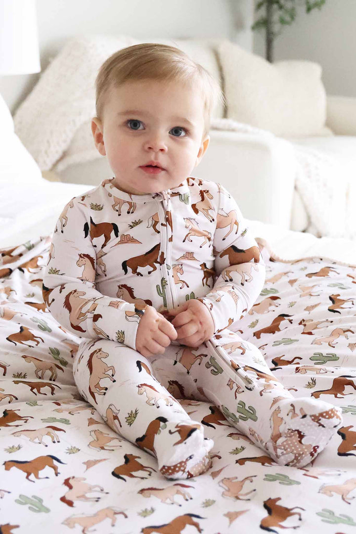 boy sitting on bed in galloping horse footie with matching blanket underneath