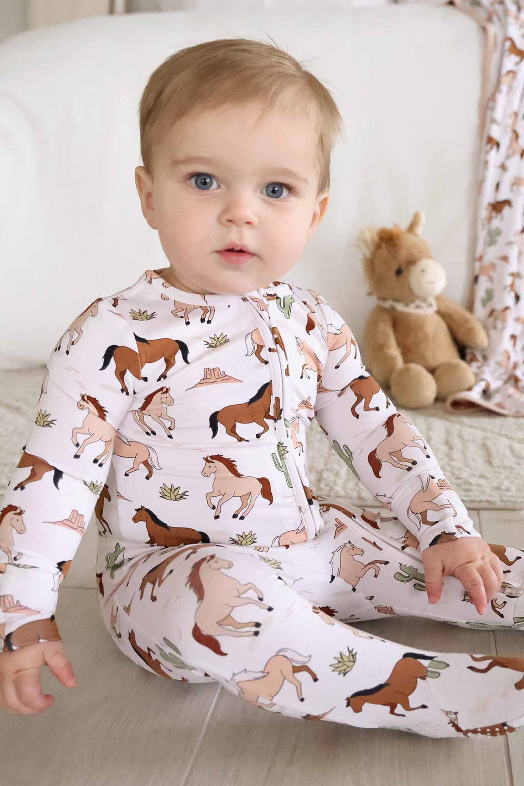 baby boy sitting on floor in neutral horse zipper footie pajama 