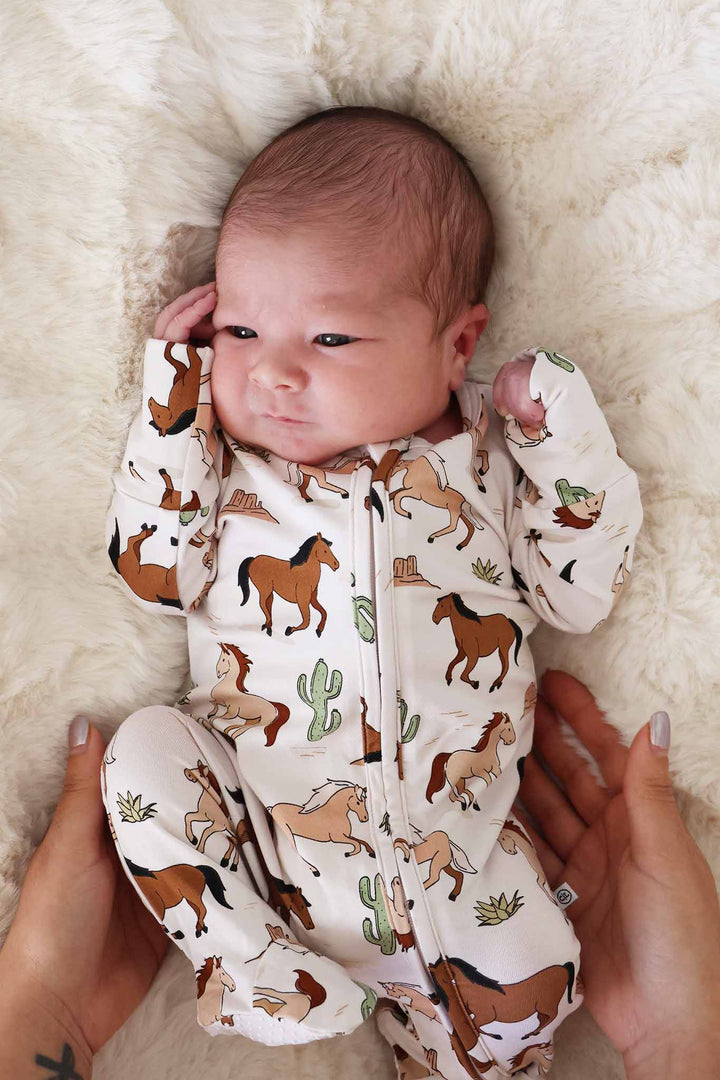newborn baby laying on blanket in galloping horse and cactus footie pajama 