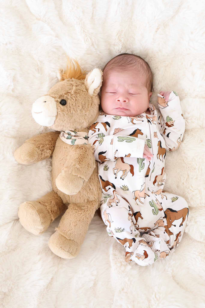 baby boy laying on fuzzy blanket next to a horse stuffed animal in a horse and cactus zipper footie 