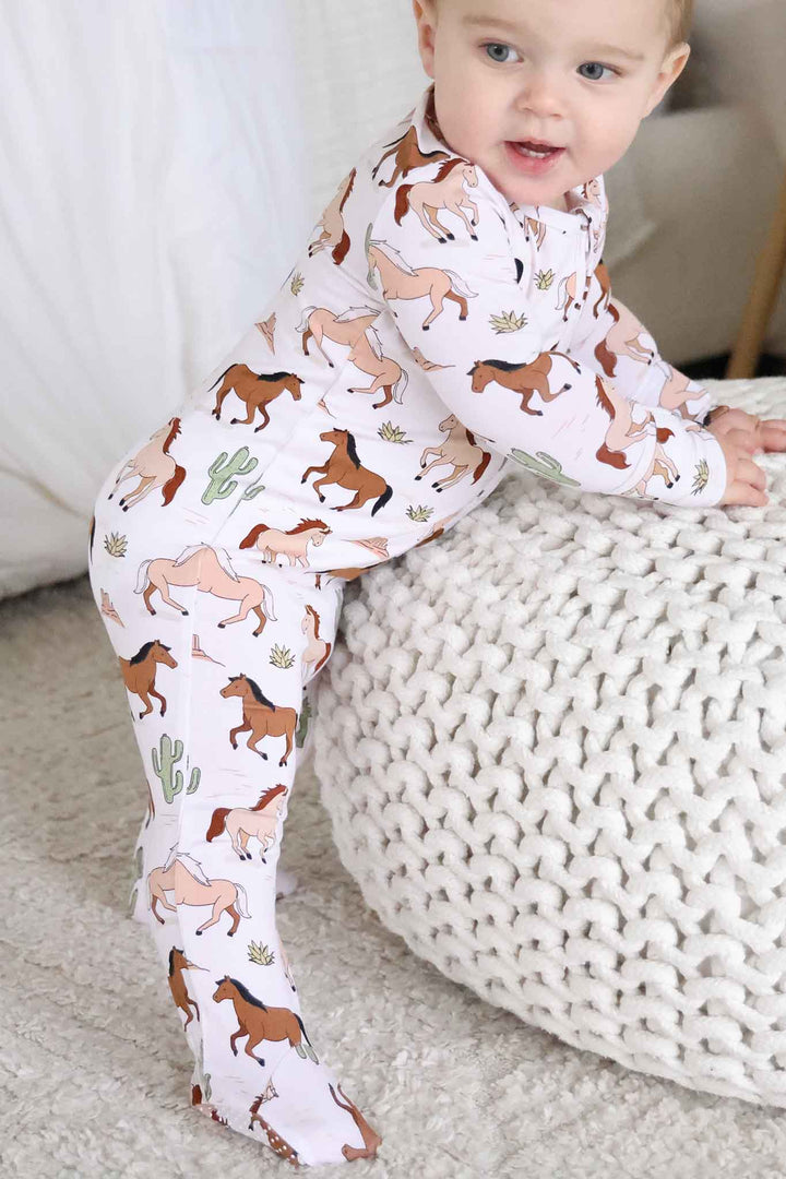 baby boy leaning against ottoman in neutral horse zipper footie pajama 