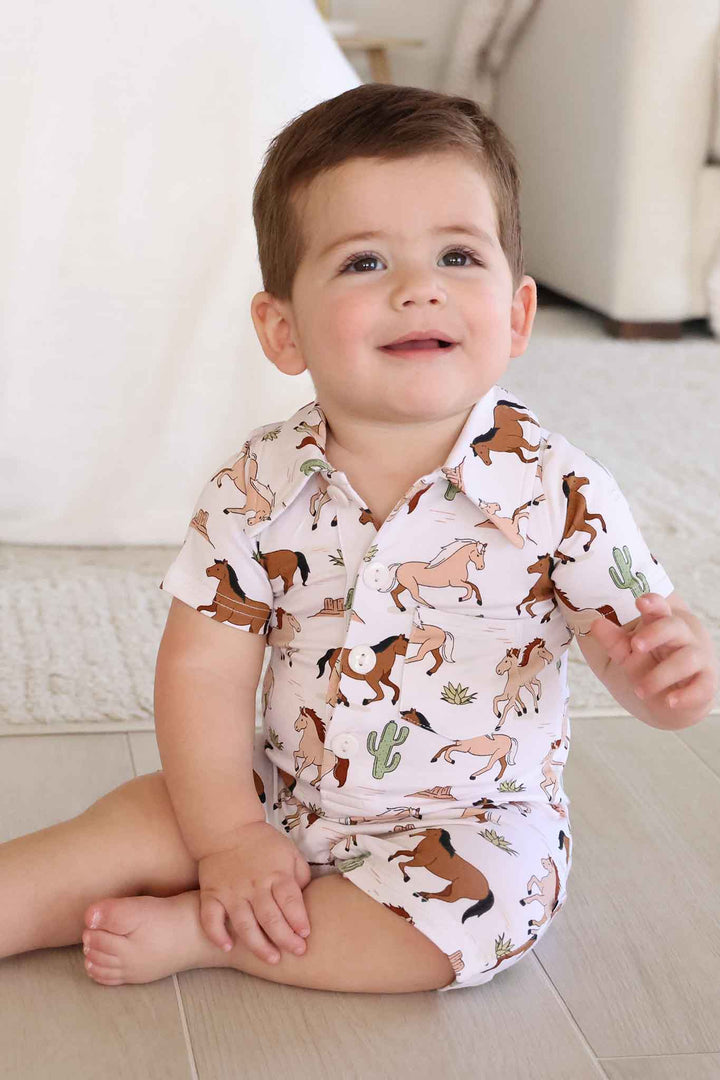 boy sitting on floor in neutral horse and cactus collared button romper