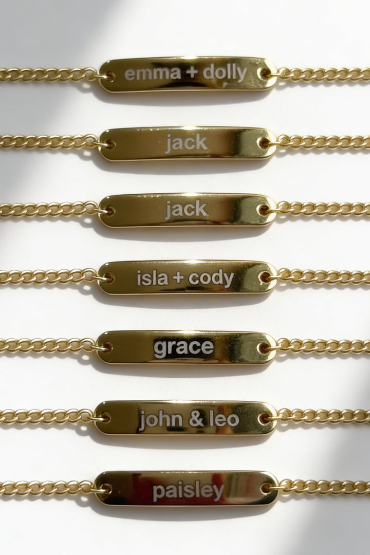 Caden Lane engraved gold bar bracelets in a row, each personalized with names like Emma + Dolly, Jack, Isla + Cody, Grace, John & Leo, and Paisley