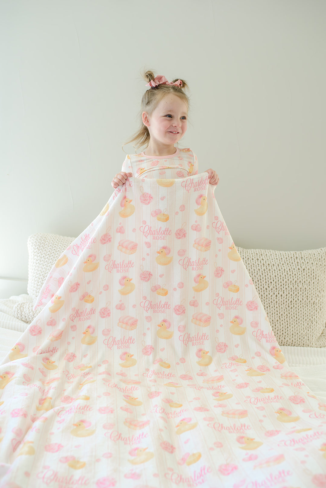 Smiling child holding pink Bubble Duckies personalized kids blanket with yellow rubber duck and custom name print