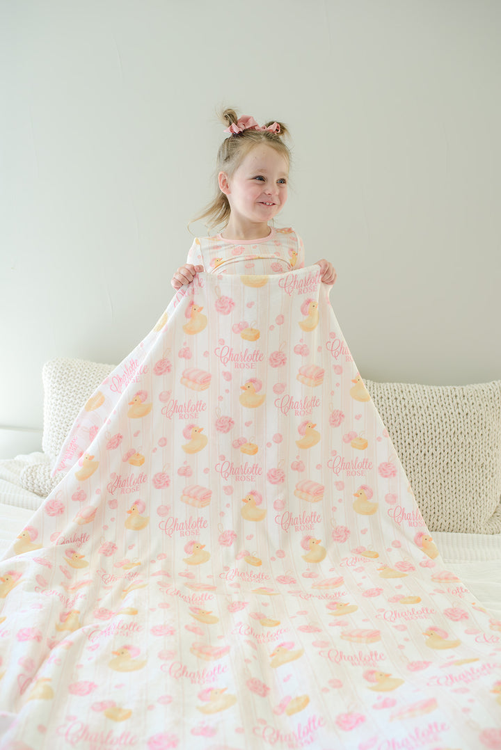 Smiling child holding pink Bubble Duckies personalized kids blanket with yellow rubber duck and custom name print