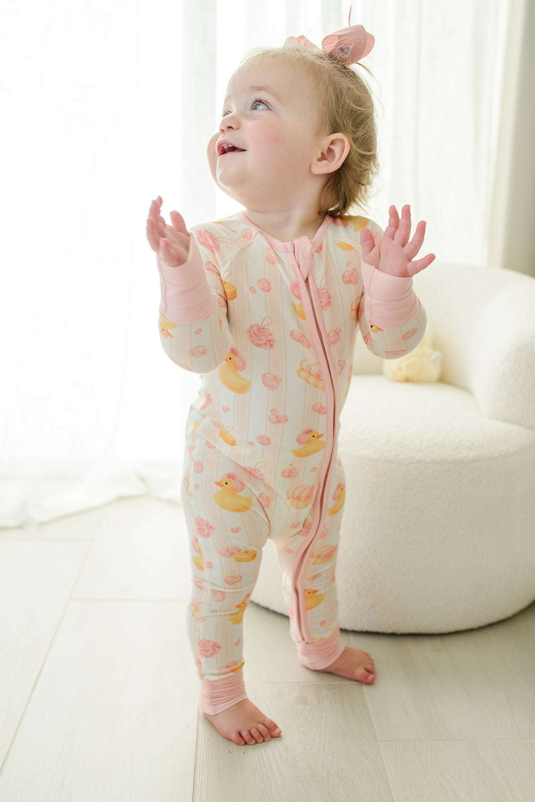 Baby girl standing in pink Bubble Duckies convertible zip romper pajamas with yellow rubber duck print