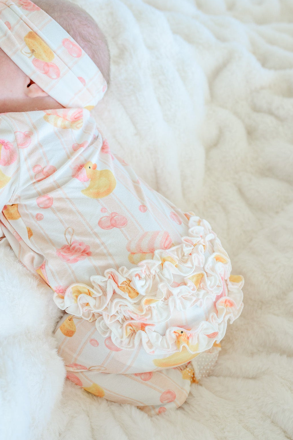 Close-up of newborn baby in pink Bubble Duckies ruffle bamboo zipper footie showing ruffle bottom detail