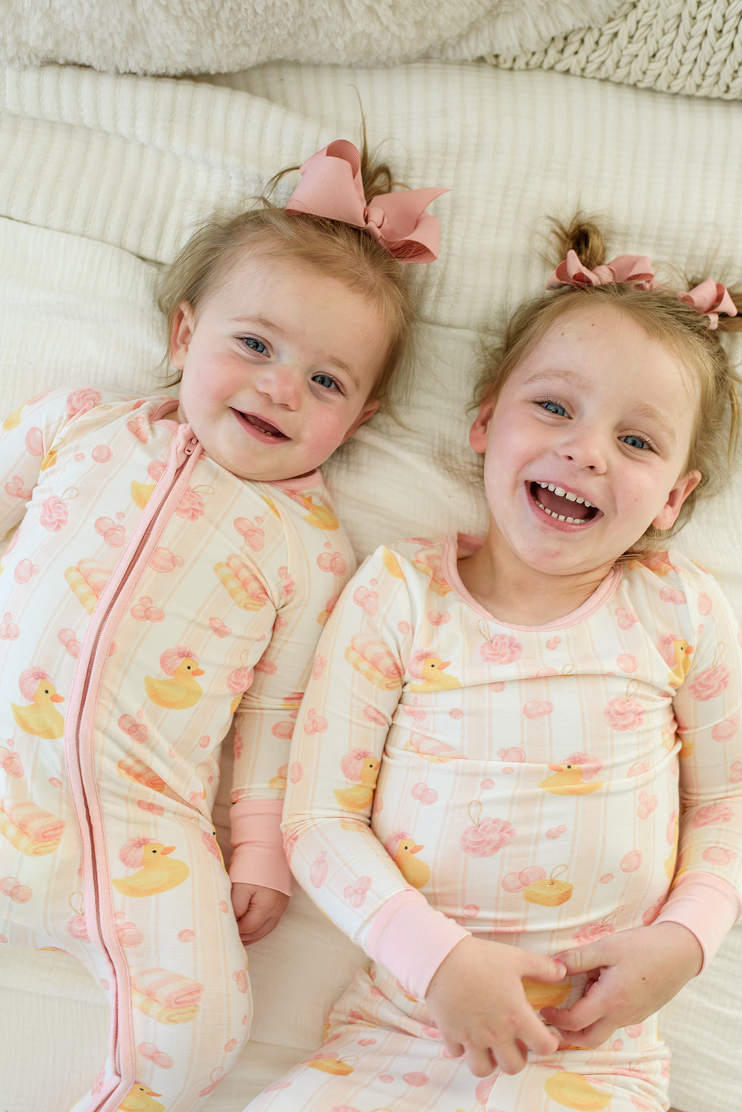 Baby girl with pink bow clapping while sitting in pink Bubble Duckies zip romper on matching duck print bedding
