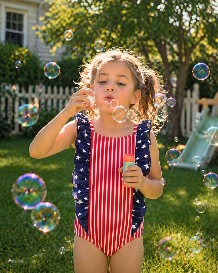 girl blowing bubbles in stars & stripes party double ruffle one piece swimsuit 