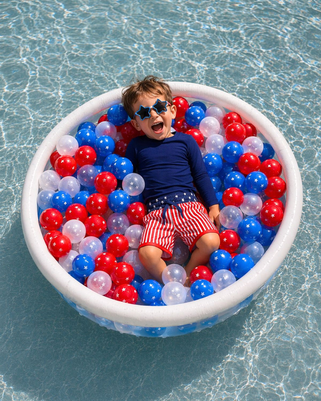 boy laying in kiddie pool with red, white and blue plastic balls