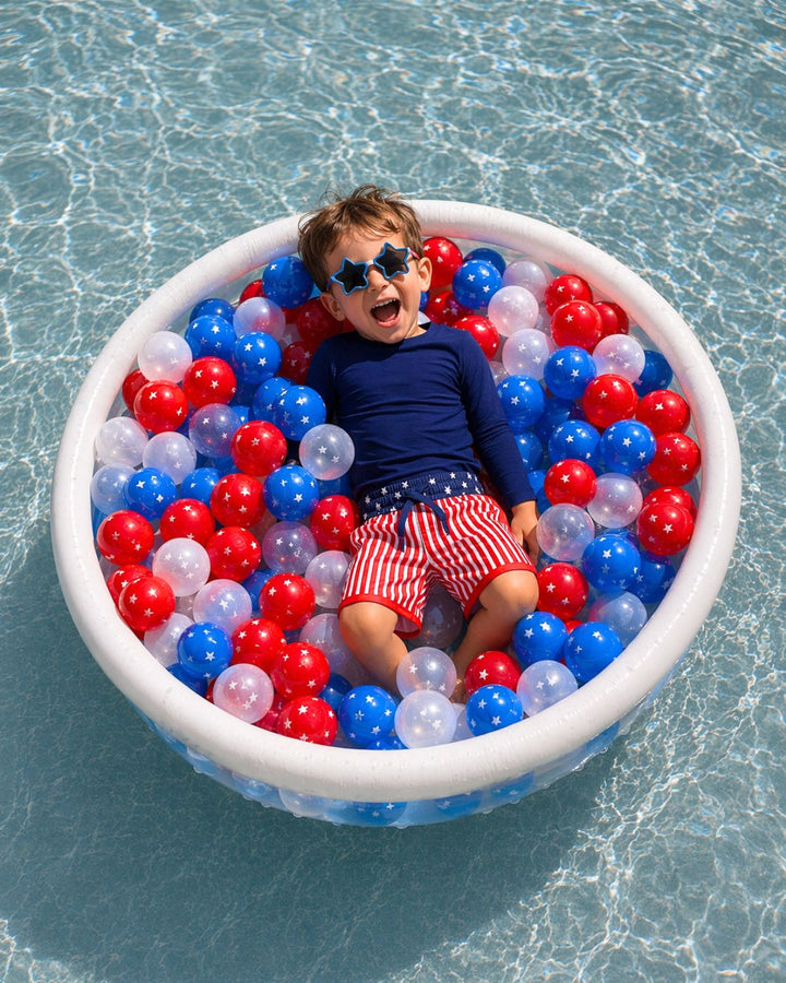 boy laying in kiddie pool with red, white and blue plastic balls